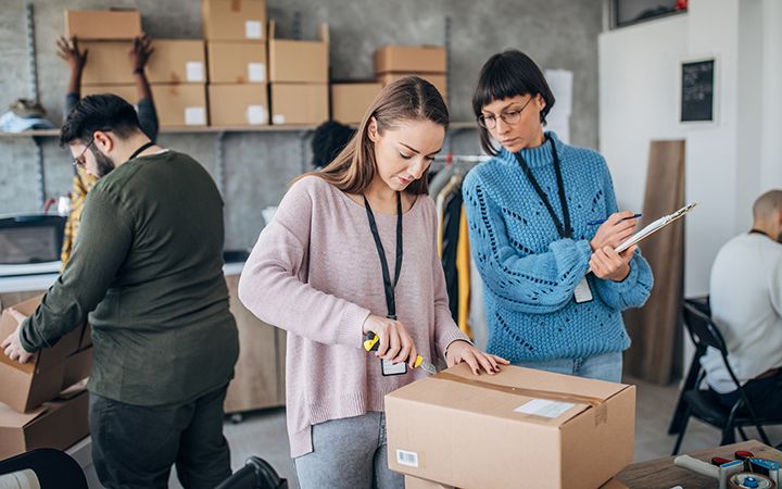 Woman opening a cardboard box while her coworker is observing that