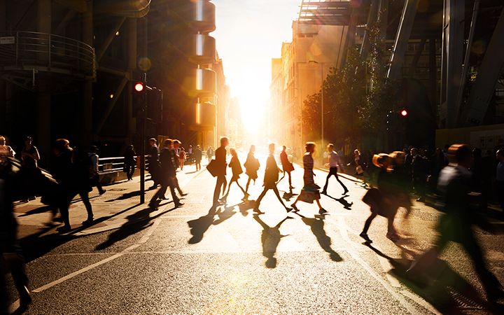 People walking past each other on a crosswalk with sunset background